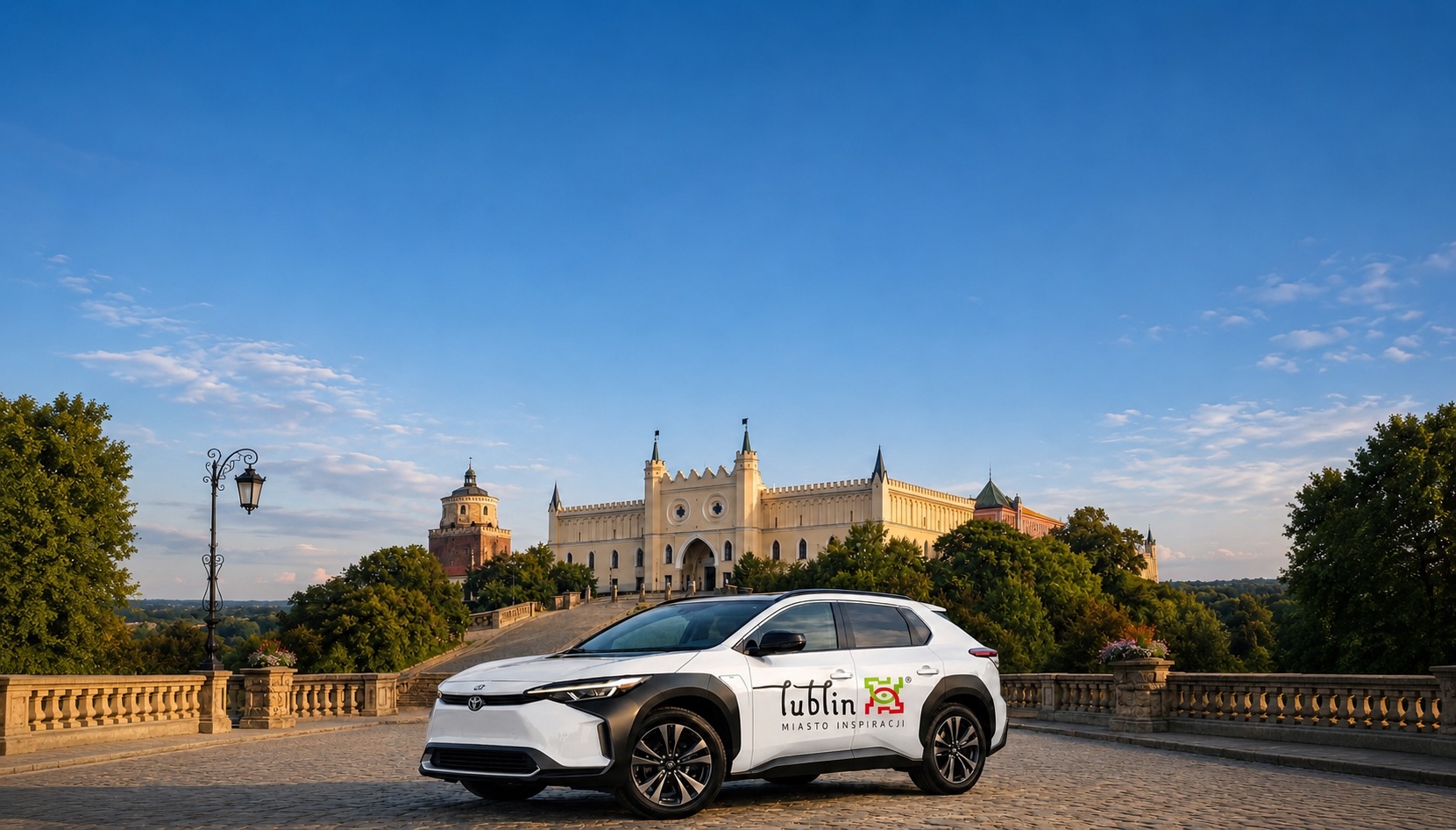 Biała Toyota bZ4X Premium Taxi Lublin na tle Zamku Lubelskiego